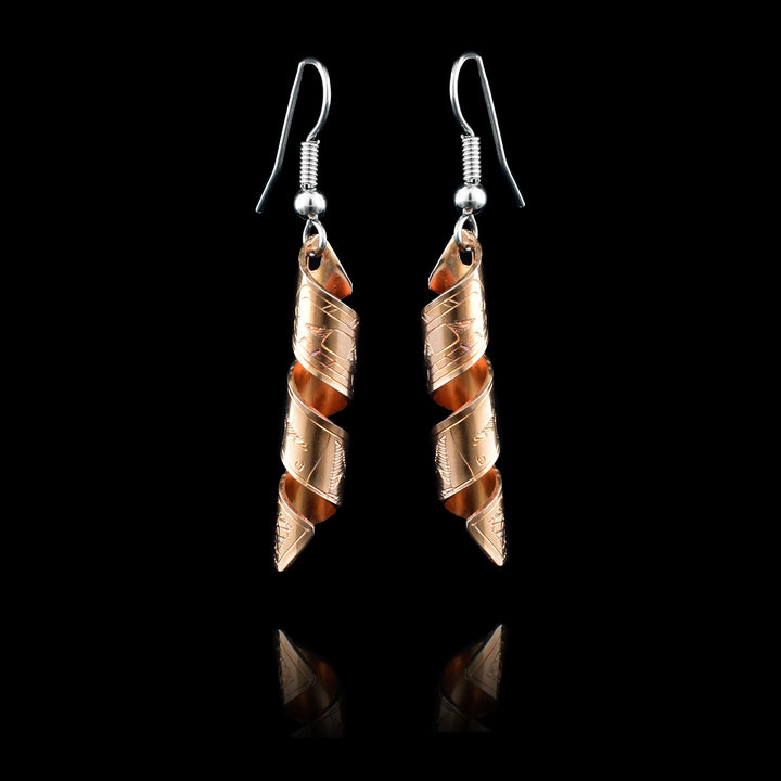 These spiral earrings have hangs made from copper bands that have been curved into horizontal spirals. The copper cylinders drop down and there is a depiction of the Orca carved into the outside of the bands. The head of the Orcas are facing the top of the piece.