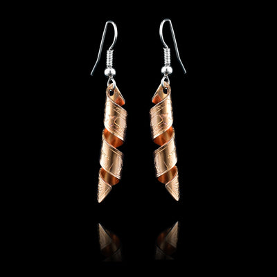 These spiral earrings have hangs made from copper bands that have been curved into horizontal spirals. The copper cylinders drop down and there is a depiction of the Orca carved into the outside of the bands. The head of the Orcas are facing the top of the piece.