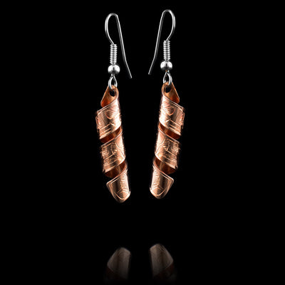 These spiral earrings have hangs made from copper bands that have been curved into horizontal spirals. The copper cylinders drop down and there is a depiction if the Wolf carved into the outside of the bands. The head of the wolf is facing the top of the piece.