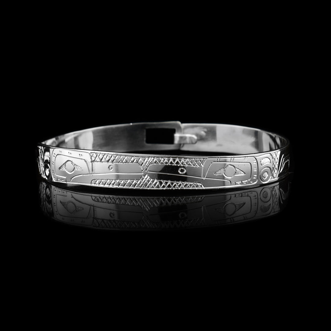 This dainty bracelet has a thin, sterling silver band with a clasp in the back. There is are depictions two Hummingbirds facing each other carved into the surface of the band. Their wings are carved behind the heads and have circular and triangular designs carved into them. There are cross hatching patterns in the background of this piece.