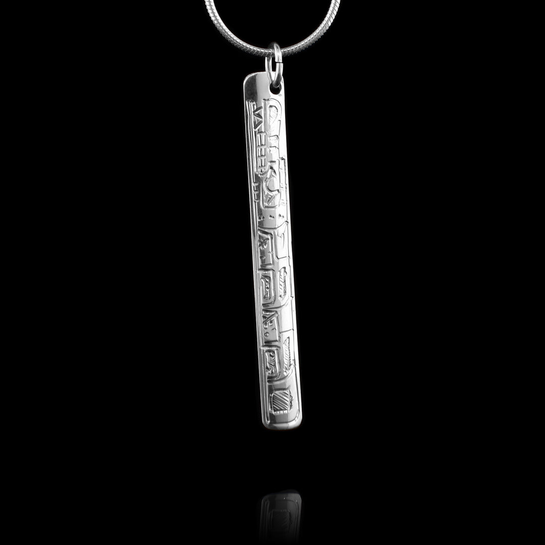 This Wolf pendant is made from sterling silver and has a long, thin shape. There are carvings on the surface of the piece depicting the Wolf.