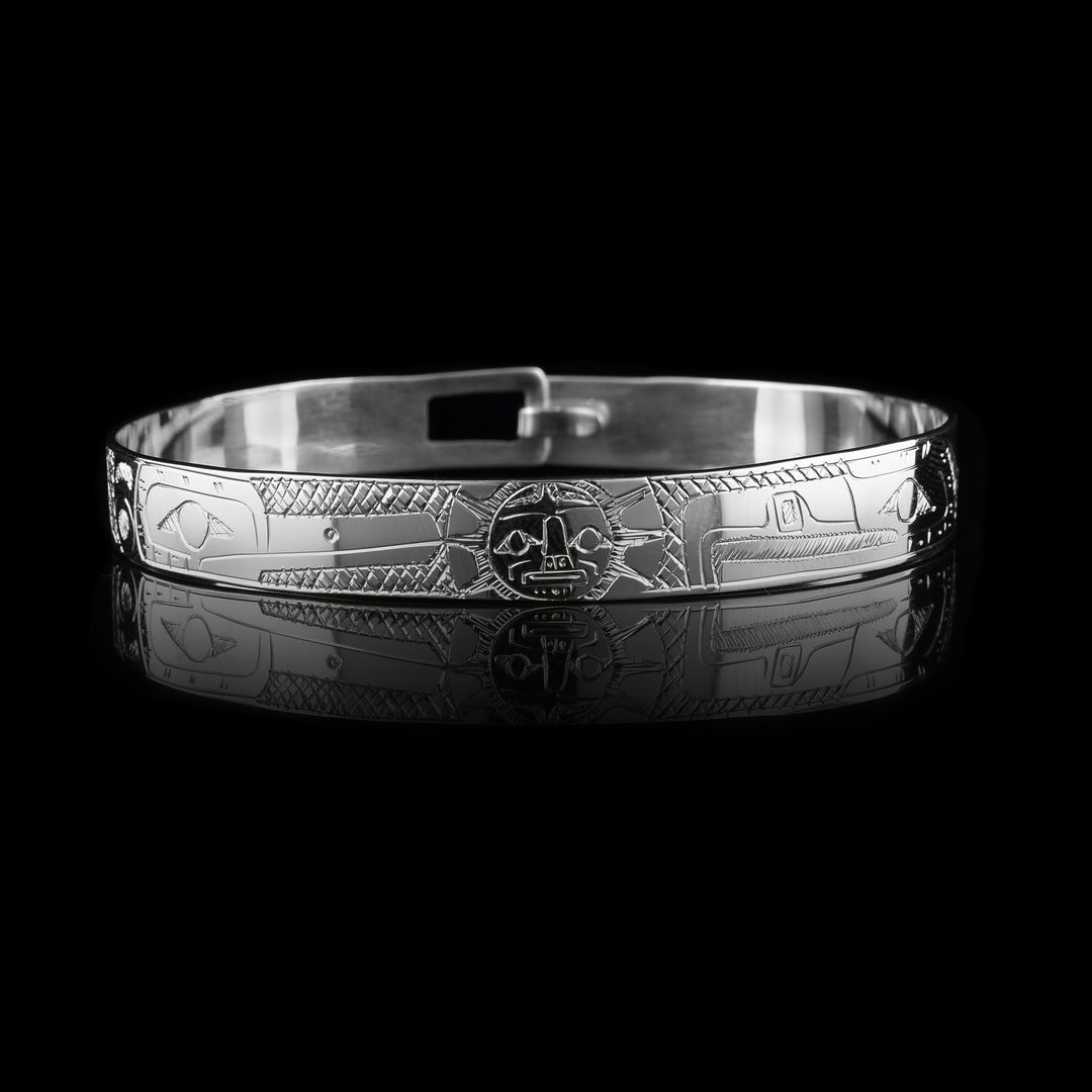 These sterling silver bangle bracelets have a single, thin band with a hook clasp in the back. There are depictions of the Eagle and the Hummingbird legends carved into either side of the band. The legends are depicted facing each other and where their heads meet, in the center, the Moon legend is depicted between them. There are cross hatching patterns in the space behind the legends.