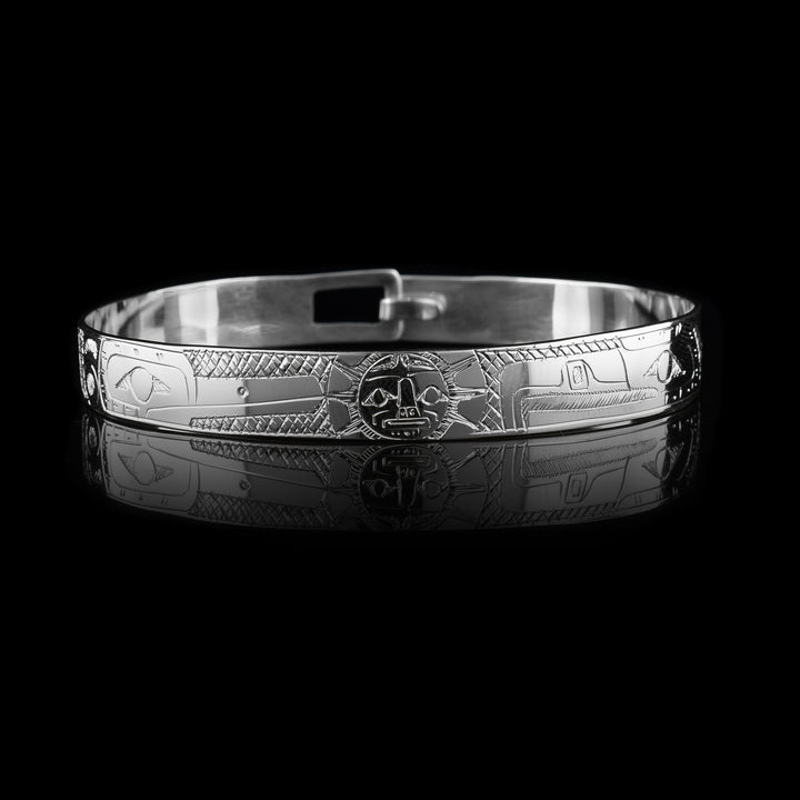 These sterling silver bangle bracelets have a single, thin band with a hook clasp in the back. There are depictions of the Eagle and the Hummingbird legends carved into either side of the band. The legends are depicted facing each other and where their heads meet, in the center, the Moon legend is depicted between them. There are cross hatching patterns in the space behind the legends.