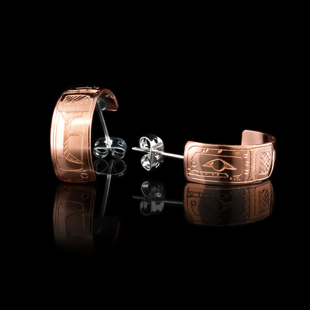 These wide hoop earrings are made from copper and have a single, wide band with a gap in the back. There are carvings on the surface of the hoops depicting the Orca. The head of the Orca takes up the entire band and is facing the hooks.