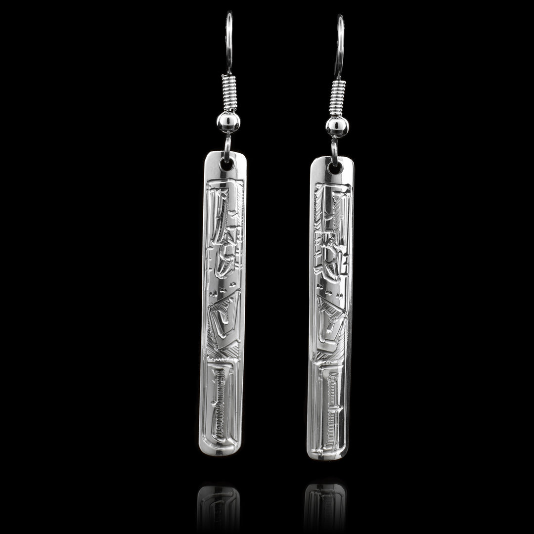 These sterling silver drop earrings have a thin, rectangular shape to them. The hangs are dangling and have carvings depicting the Eagle on the surface of them.