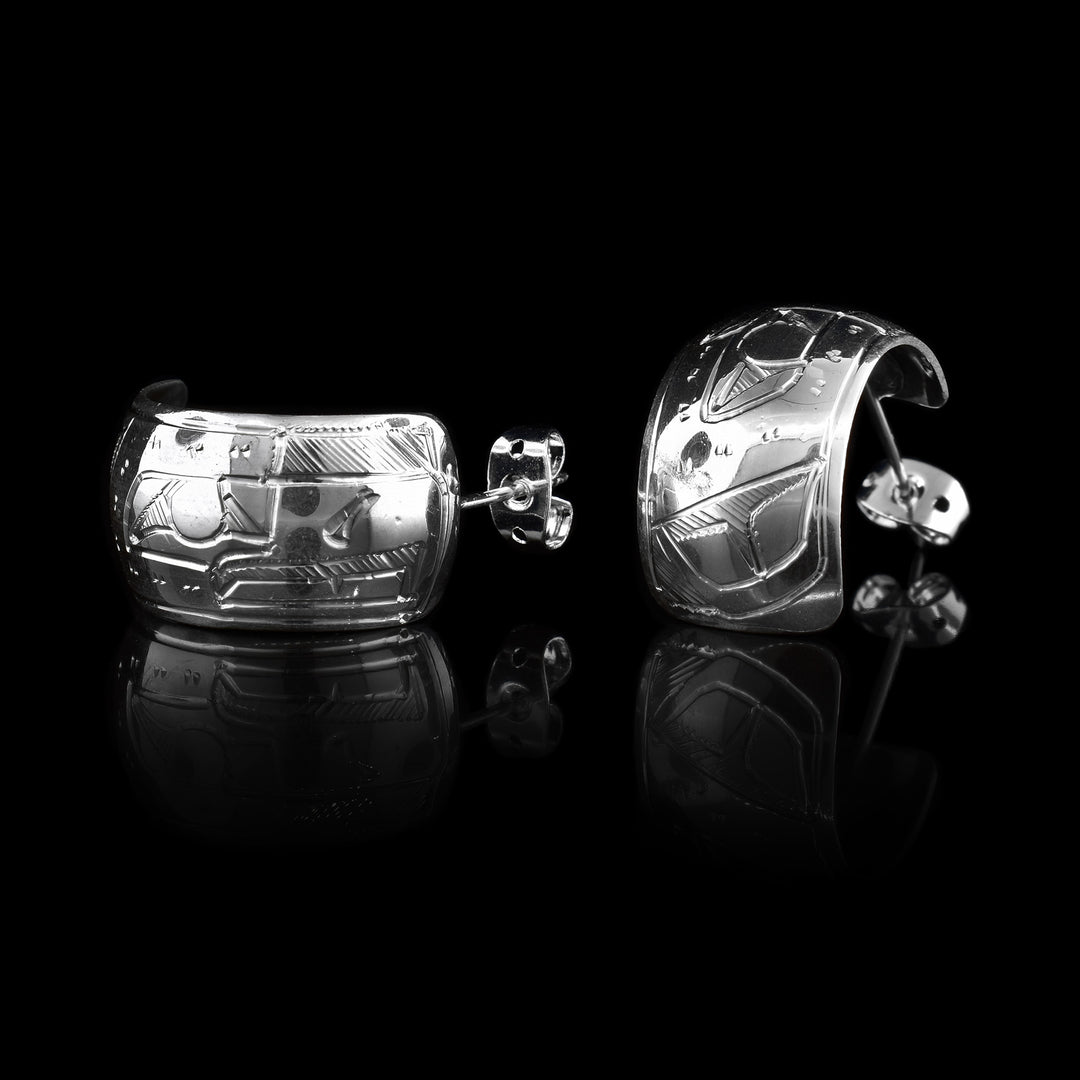 These wide hoop earrings are made from sterling silver and have a single, wide band with a gap in the back. There are carvings on the surface of the hoops depicting the Eagle.