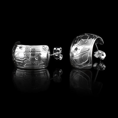 These wide hoop earrings are made from sterling silver and have a single, wide band with a gap in the back. There are carvings on the surface of the hoops depicting the Eagle.