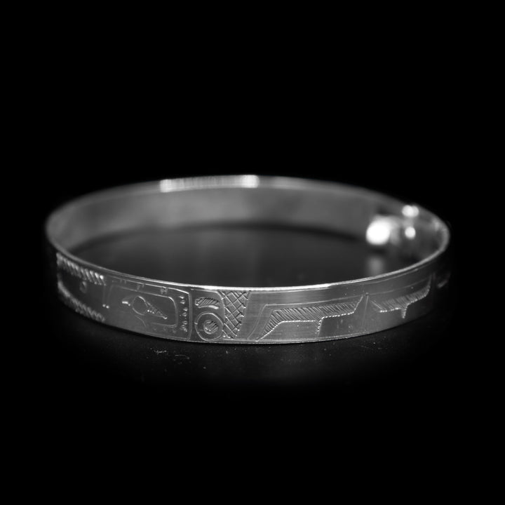 This large bangle Hummingbird bracelet has a thin, sterling silver band with a clasp in the back. There are depictions of the Hummingbird facing each other carved into the piece. There is also a flower carved into the center of the piece.