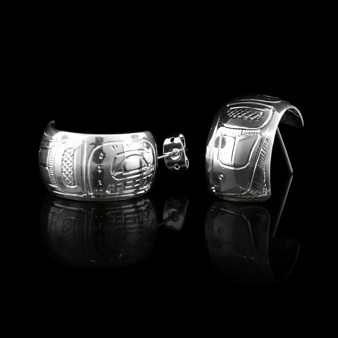 These wide hoop earrings are made from sterling silver and have a single, wide band with a gap in the back. There are carvings on the surface of the hoops depicting the Orca.