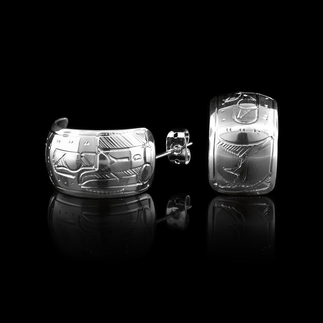 These wide hoop earrings are made from sterling silver and have a single, wide band with a gap in the back. There are carvings on the surface of the hoops depicting the Raven.