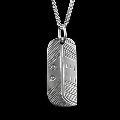 This feather pendant is made form sterling silver and has a wide and rectangular shape to it. There are intricate carvings made across the surface of it depicting a feather.