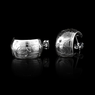These wide hoop earrings are made from sterling silver and have a single, wide band with a gap in the back. There are carvings on the surface of the hoops depicting the Thunderbird.