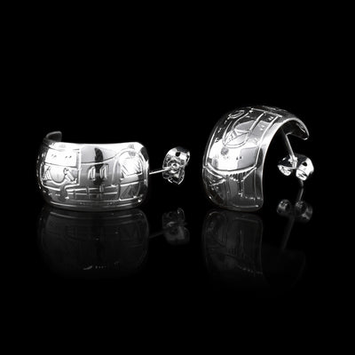These wide hoop earrings are made from sterling silver and have a single, wide band with a gap in the back. There are carvings on the surface of the hoops depicting the Wolf.