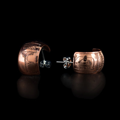 These copper hoop earrings have wide bands made from copper that are rounded and concaved. The bands for m small, half circles and there is a depiction of the Orca's head carved into them. The nose, teeth and eyes are shown and the head is facing the studs.