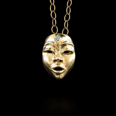 This blue topaz pendant is made from brass and has been embossed to depict the face of the fenimide Seer. There are eyes, mouth, eyebrows and a distinct face shape that make up the pendant. The gem is set on the forehead of the Seer.