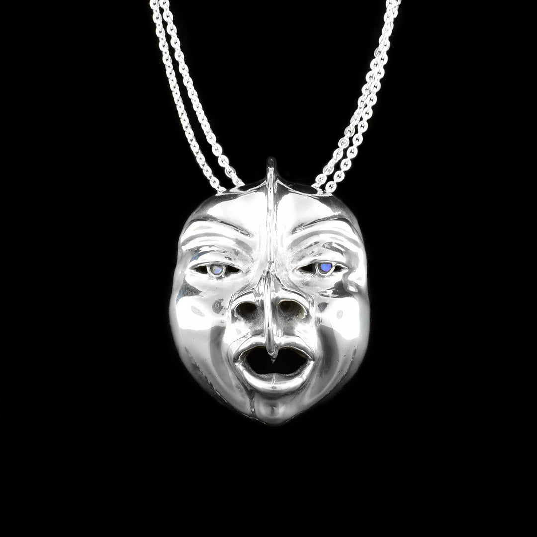 This sterling silver pendant is shaped like a face with detailed eyes, cheeks, lips, eyebrows, and nose. The are abalone gemstones set into they eyes of the mask.
