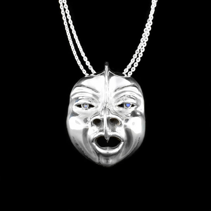 This sterling silver pendant is shaped like a face with detailed eyes, cheeks, lips, eyebrows, and nose. The are abalone gemstones set into they eyes of the mask.