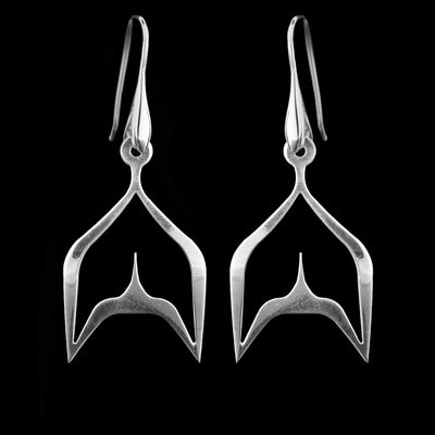 These sterling silver dangling earrings have thin hangs that split into a whale tail shape and depict a Haida Gwaii character.