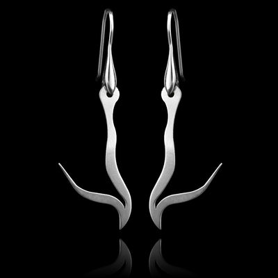 These sterling silver long dangling earrings have thin hangs that drop down and have points protruding from them. The hangs depict a Haida Gwaii character.