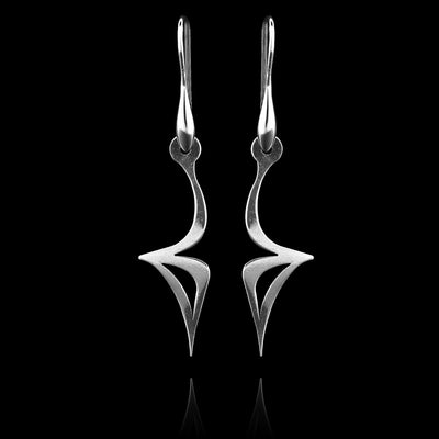 These sterling silver long dangling earrings have thin hangs that drop down. They curve out sharply in the center and have cutout, triangle pieces with sharp ends at the bottom. The hangs depict a Haida Gwaii character.
