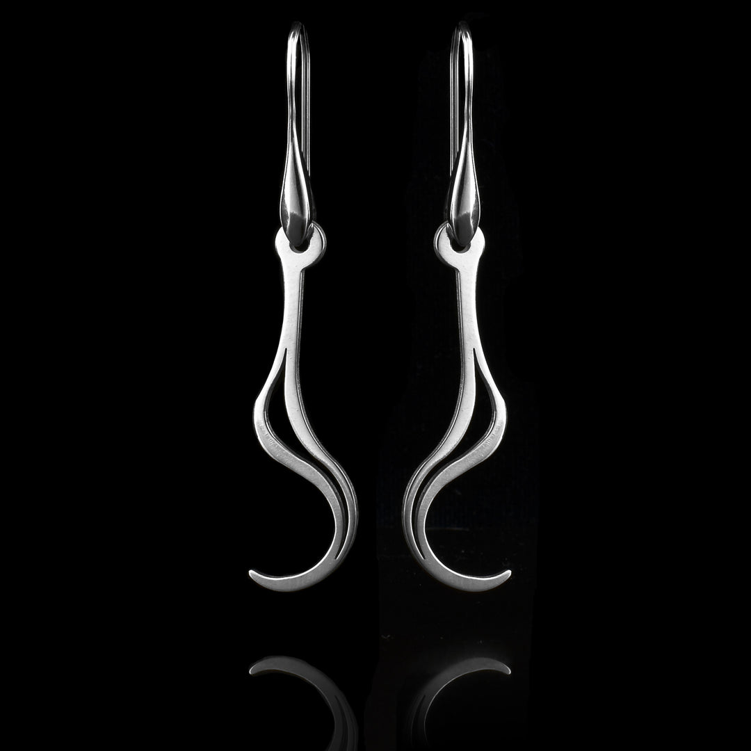 These sterling silver long dangling earrings have thin hangs that drop down and curve up at the ends. There is a cutout, teardrop shape in the center of them The hangs depict a Haida Gwaii character.