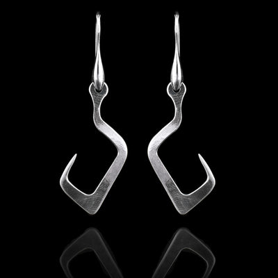 These sterling silver long dangling earrings have thin hangs that drop down and curve upwards. The curves of the hooks are squared. The hangs depict a Haida Gwaii character.