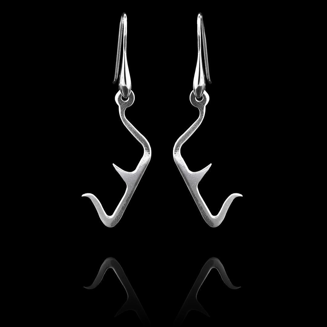 These sterling silver long dangling earrings have thin hangs that drop down and have points protruding from them. The hangs depict a Haida Gwaii character.