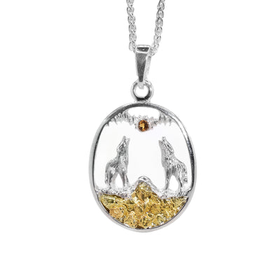 Cut out pendant with sterling silver wolves howling at faceted, orange citrine moon. Wolves are in a mountainous landscape made of 22K gold nuggets. Oval sterling silver frame and bail.