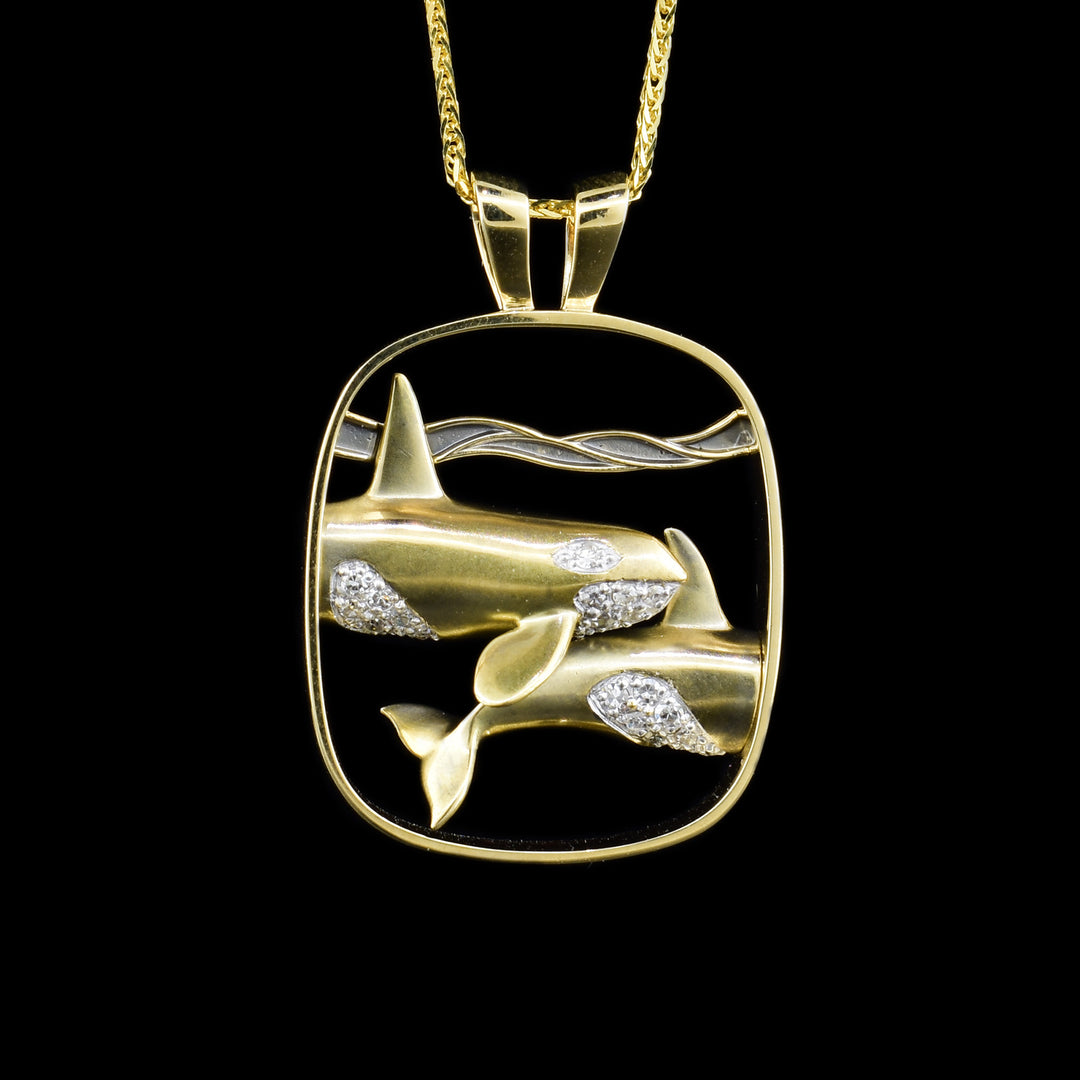 14K yellow and white gold pendant featuring diamond-encrusted orcas swimming underwater. Cut out background. Handcrafted by Dennis Kangasniemi.
