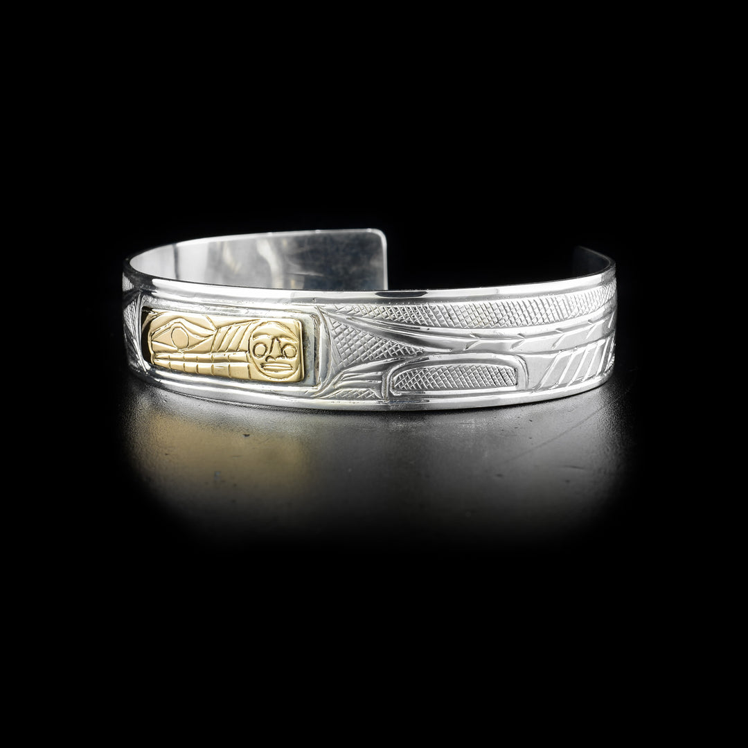 Depicts 14K yellow gold rectangle with wolf and moon on front. Rest of piece is sterling silver and has carved designs with cross-hatching background. By Heiltsuk artist Reg Gladstone.