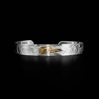 Sterling silver bracelet with 14K yellow gold hummingbird head facing left. Hummingbird’s body begins on right side and flowers begin on left. Design done in ovoids and lines. Cross-hatching background.