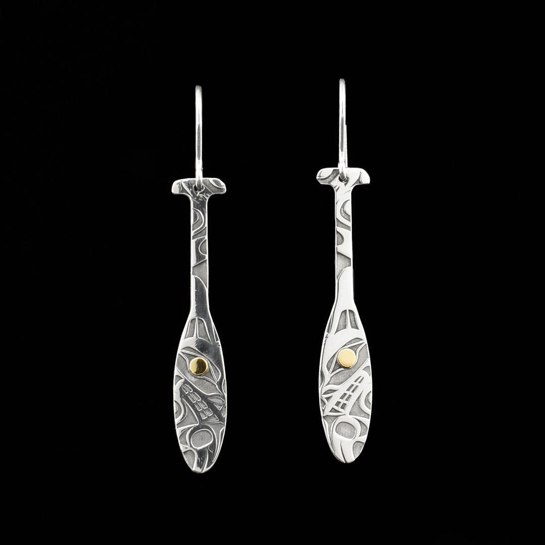 Dangle earrings in shape of Tahltan paddles. Both paddles have a side-view of a wolf’s head and a paw with designs above. 18K gold in the pupils.