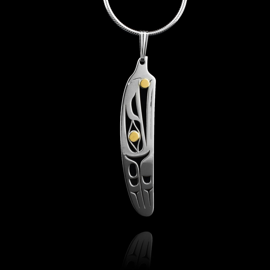 This Raven feather pendant is crafted from sterling silver with elegant 14K gold accents. Shaped like a feather, the pendant features detailed cutouts that depict the Raven legend, with the Raven’s head positioned at the top, facing upward. Behind the head is a wing-like feather design, adding depth and movement to the piece. A 14K gold circle represents the Raven’s eye, while another gold accent highlights the gold pearl held in its beak.