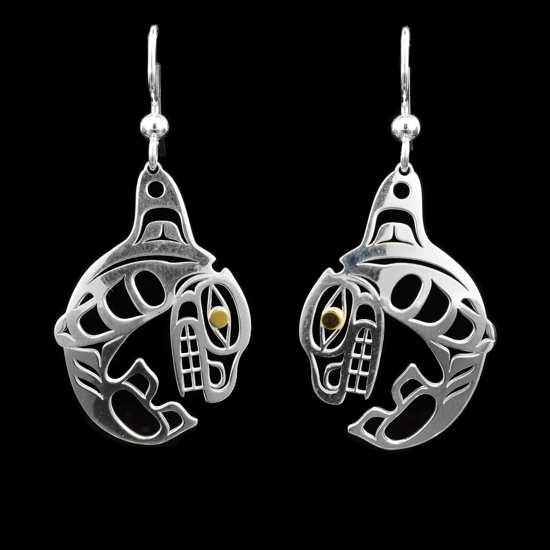 These dangling Orca earrings are made from sterling silver and 14K gold. The hangs are shaped like and have cutouts on them depicting the Orca; the eyes of the legends are made from gold.