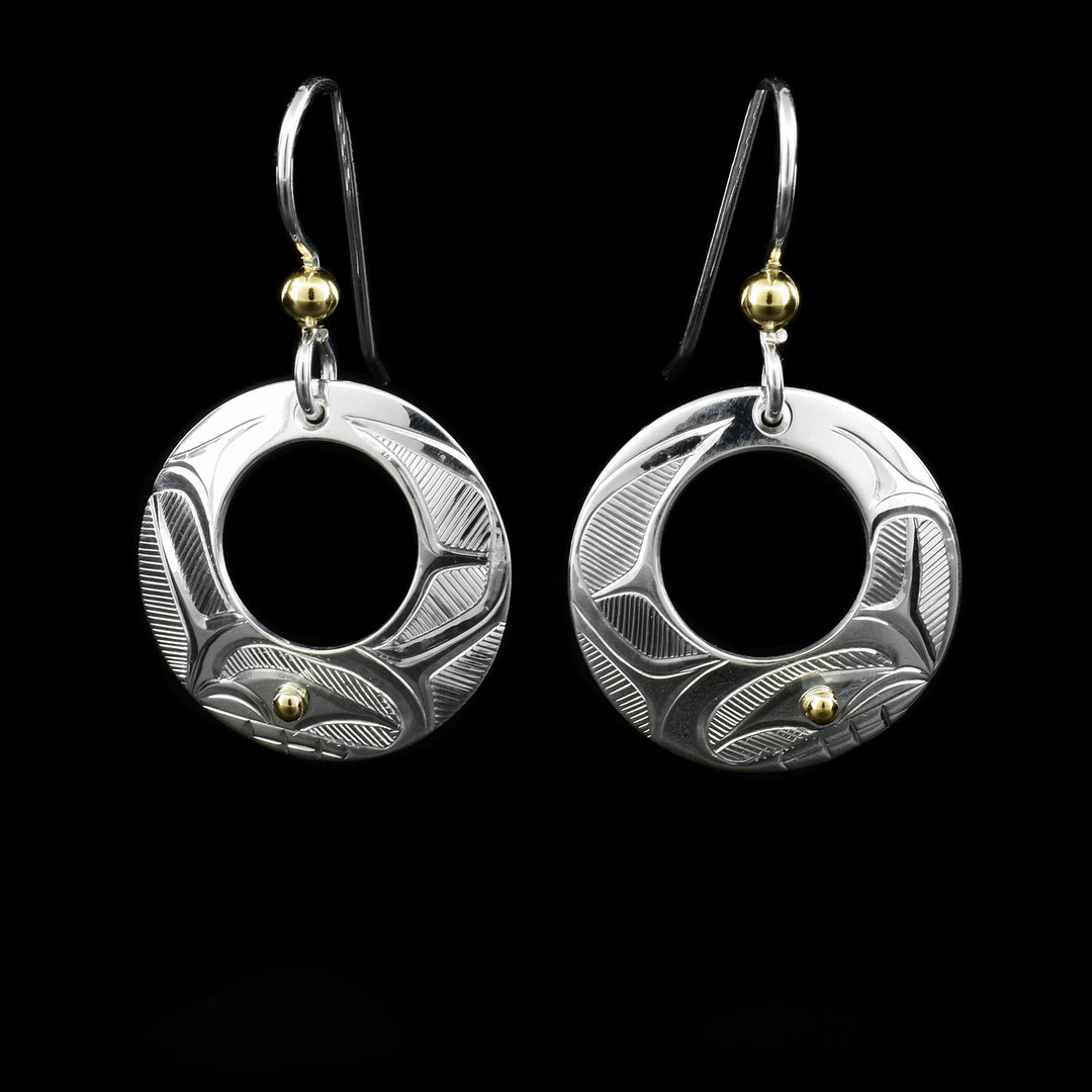 These sterling silver earrings have circle hangs with circle cutouts. There are depictions of the Orca carved into the surface. There are 14K gold balls in the eyes of the Orca and attached to the hooks.