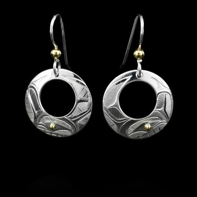 These sterling silver earrings have circle hangs with circle cutouts. There are depictions of the Orca carved into the surface. There are 14K gold balls in the eyes of the Orca and attached to the hooks.