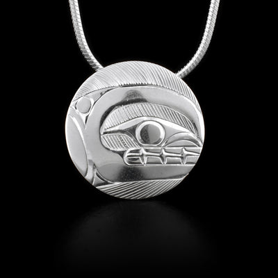 This sterling silver pendant is circle shaped. There is a depiction of the Orca carved into it.