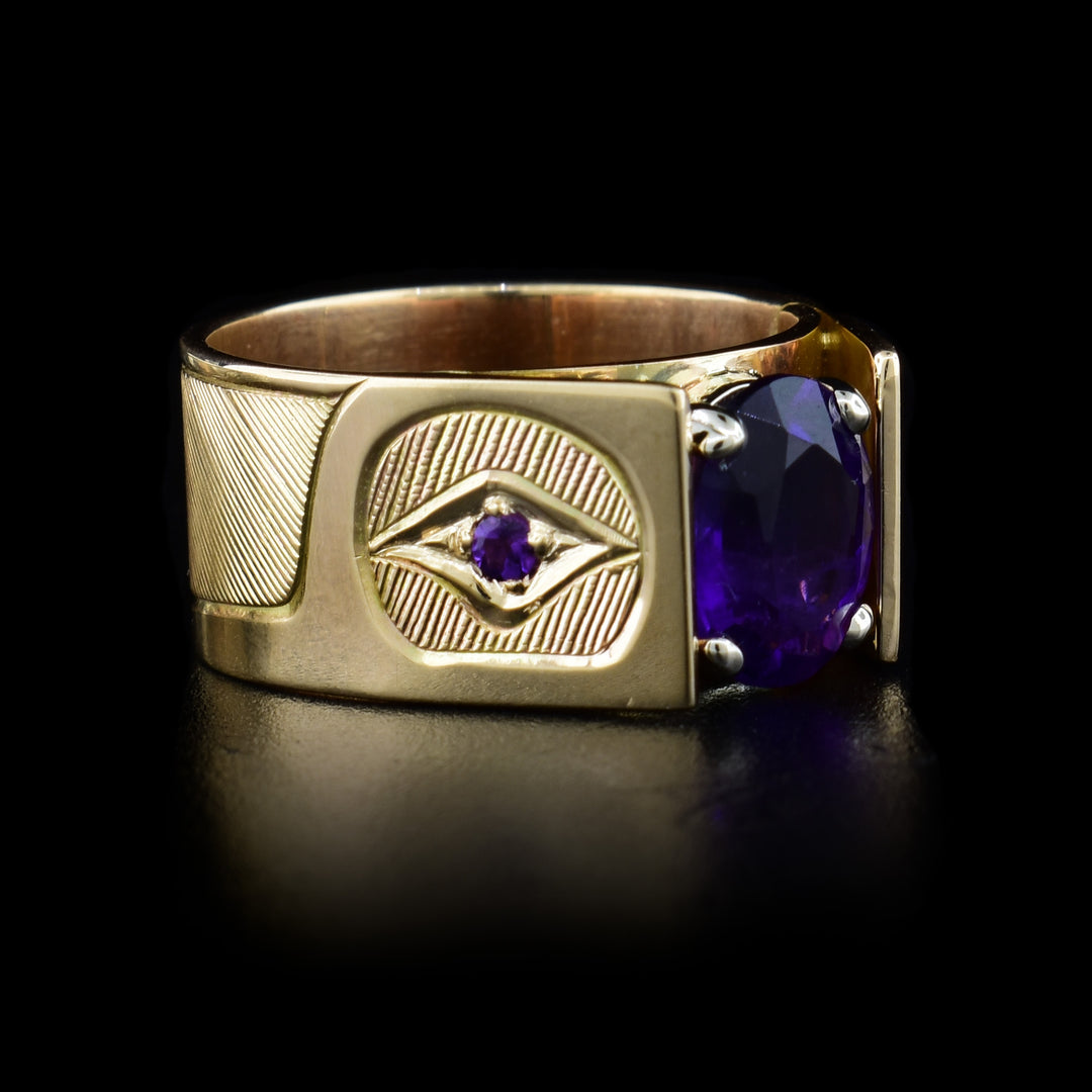 This cathedral solitaire amethyst ring is made from 14K gold and has a depiction of the Hummingbird carved into the band. The head of the Hummingbird is carved by the gem and its beak faces down on the band. The band extends up and frames the large, amethyst gem. There is also a small, amethyst embedded in the eye of the legend.