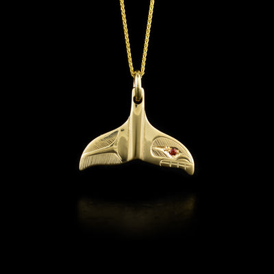 This 14K gold whale tail necklace pendant is shaped like a whale's tail and has a depiction of the Orca carved into the surface of the piece. There is a garnet gemstone set into the eye of the Orca.