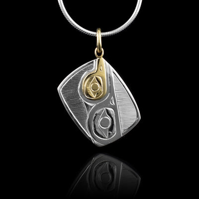 This sterling silver and 14K gold Hummingbird pendant is small and has a rectangle shape to it. The piece hangs from one of its corners with a gold jump ring. There are beautiful carvings made across the surface of the pendant depicting the Hummingbird. The head of the legend is done in gold.