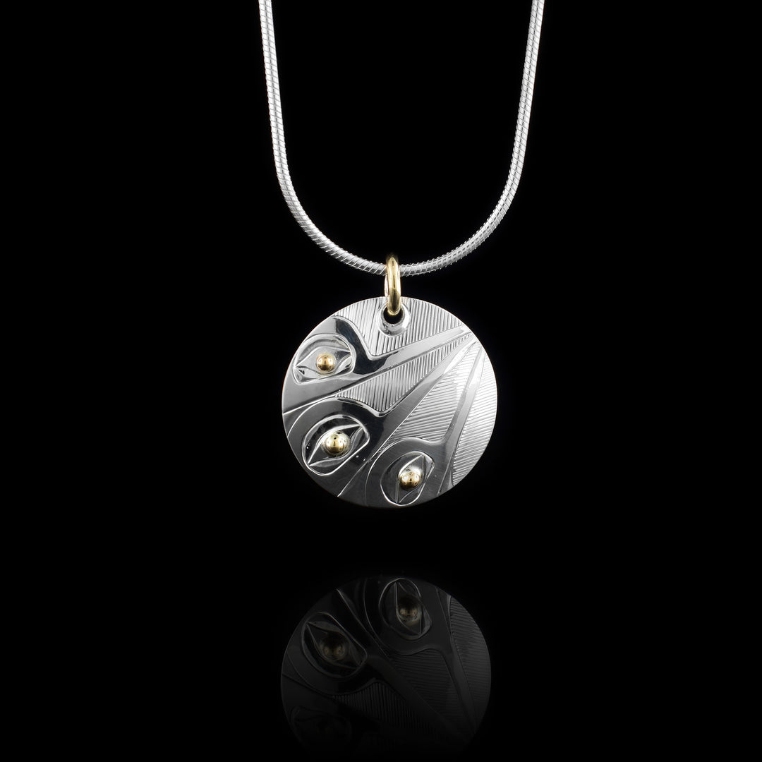 This sterling silver and 14K gold Hummingbird pendant is circle shaped and has three depictions of the Hummingbird carved into the piece. The legends have their beaks raised and they meet at the top of the pendant.