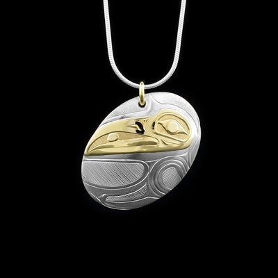This Raven pendant is made from sterling silver and 14K gold and has an oval shape. The pendant is chunky and has carvings of the surface of it that depict the Raven and the head of the Raven is made from gold.