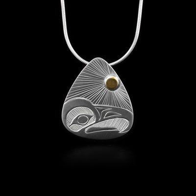 This Eagle pendant is teardrop shaped and made from sterling silver. There is a carving of the Eagle carved into the surface of the piece and a 14K gold stud representing the sun in the top of the piece. The head of the Eagle is carved in a side profile at the bottom of the piece and there are sun rays extending across the piece from the gold stud.