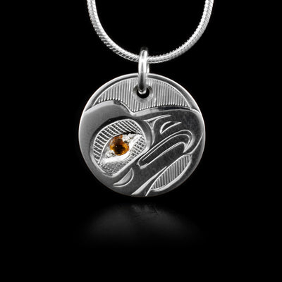 This sterling silver Eagle pendant is small and circle shaped. There is a depiction of the Eagle carved into it. There is also a citrine gem embedded in the eye of the Eagle.