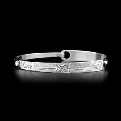 This Hummingbird bracelet is made from sterling silver and has a thin, tapered band with a clasp in the back. There are two depictions of the Hummingbird facing a flower carved into the surface of the band.