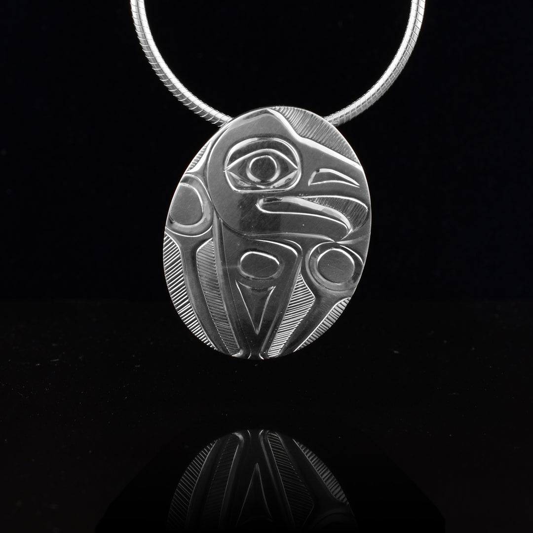 This sterling silver oval pendant is small in size and has a depiction of the Eagle legend carved into it. The Eagle head is in a side profile at the top and its wings are in front of him at the sides. There are thin, symmetrical lines giving feather details to the wings.