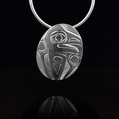 This sterling silver oval pendant is small in size and has a depiction of the Eagle legend carved into it. The Eagle head is in a side profile at the top and its wings are in front of him at the sides. There are thin, symmetrical lines giving feather details to the wings.