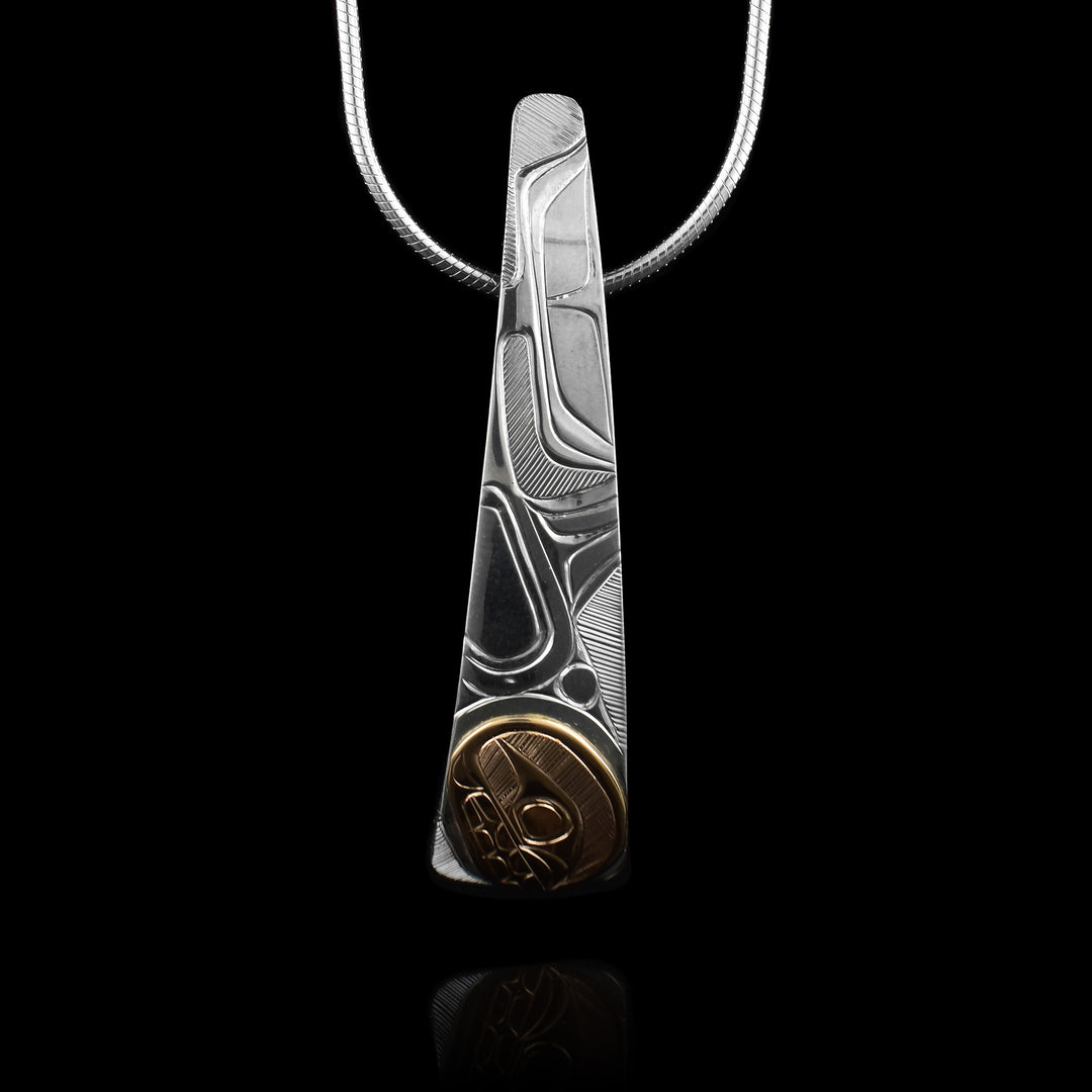 This Orca whale pendant is made from sterling silver, is long and vertical. The piece gradually tapers and forms a slight, long teardrop shape; also there is a slight curve to it in a convex fashion. The Orca head is carved in a 14K gold circle at the bottom of the piece. Details like its body, dorsal fin and tail are carved higher up on the piece.