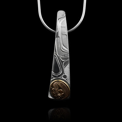 This Orca whale pendant is made from sterling silver, is long and vertical. The piece gradually tapers and forms a slight, long teardrop shape; also there is a slight curve to it in a convex fashion. The Orca head is carved in a 14K gold circle at the bottom of the piece. Details like its body, dorsal fin and tail are carved higher up on the piece.