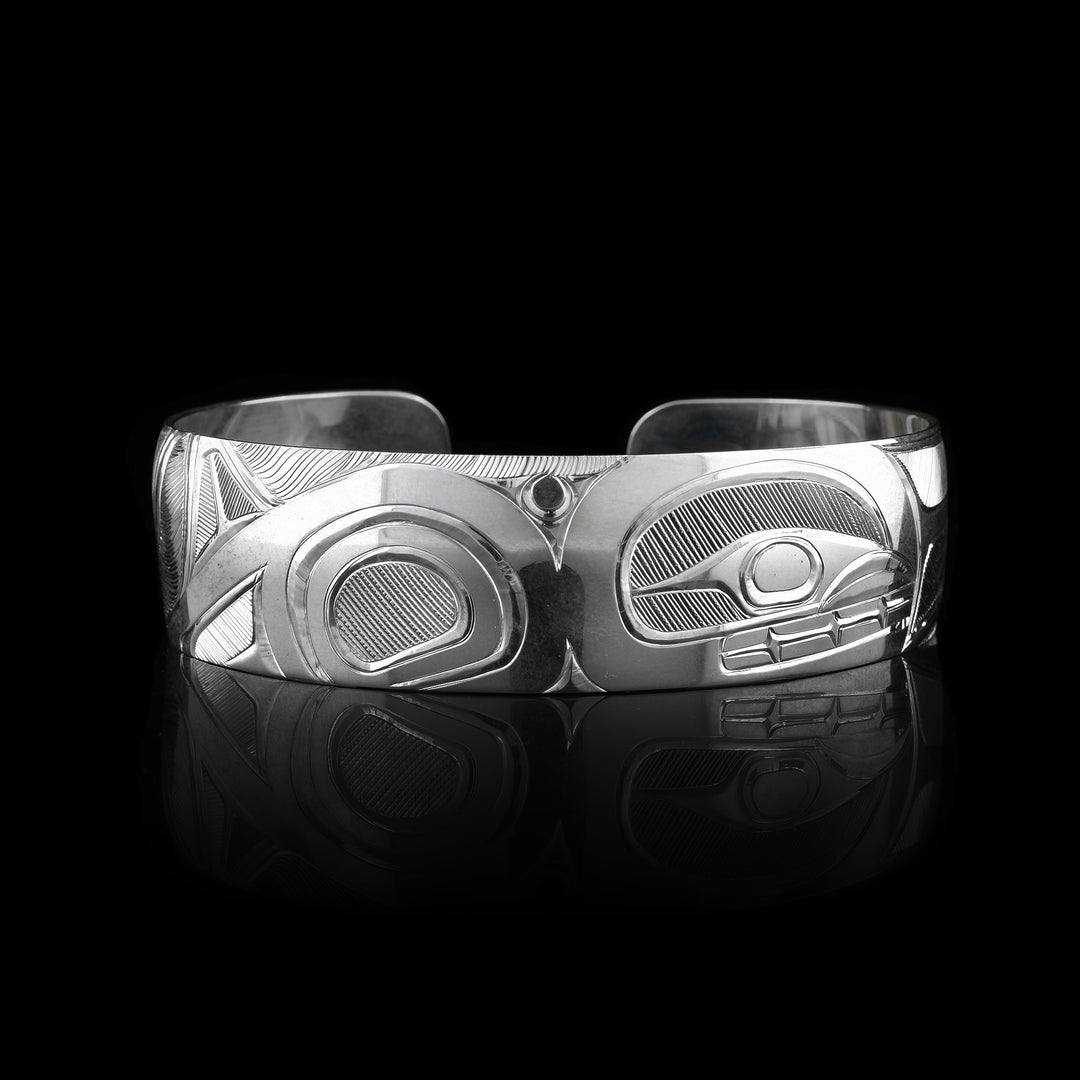 This elegant Orca bracelet cuff has a wide, sterling silver band with a gap in the back. The Orca's head and torso are carved in a side profile in the center of the band. To the left of the piece, the rest of its body is depicted. There are fine, line patterns emphasizing the details of the piece.